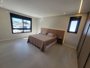 Ein modernes Schlafzimmer mit einem großen Bett, einem Nachttisch, einem an der Wand befestigten Fernseher und einem Fenster mit Blick auf Gebäude.