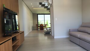 Un salon moderne avec un canapé, un téléviseur posé sur un meuble en bois et un coin repas comprenant une table et des chaises.