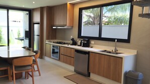Une cuisine moderne avec des meubles en bois, un réfrigérateur en acier inoxydable, un lave-vaisselle et une fenêtre donnant sur un espace verdoyant.