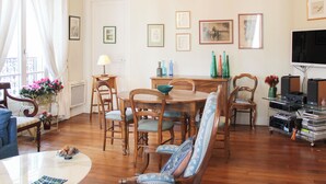 A living room with a dining table, chairs, a sofa, a TV, and a bookshelf. - Timeless apartment in a Haussmannian building (Paris)