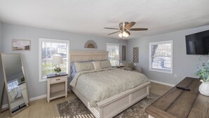 Une chambre à coucher comprenant un lit, des tables de chevet, une commode, un ventilateur de plafond et un téléviseur.