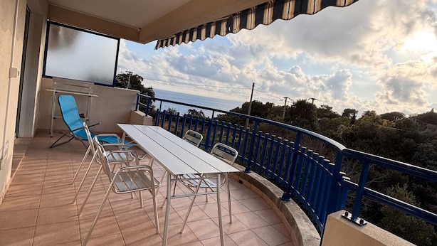 Ein Balkon mit Tisch und Stühlen, einem blauen Geländer und Blick auf das Meer.