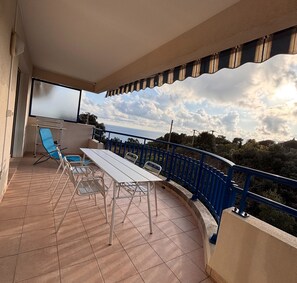 Un balcon avec une table et des chaises, une rambarde bleue et une vue sur la mer.