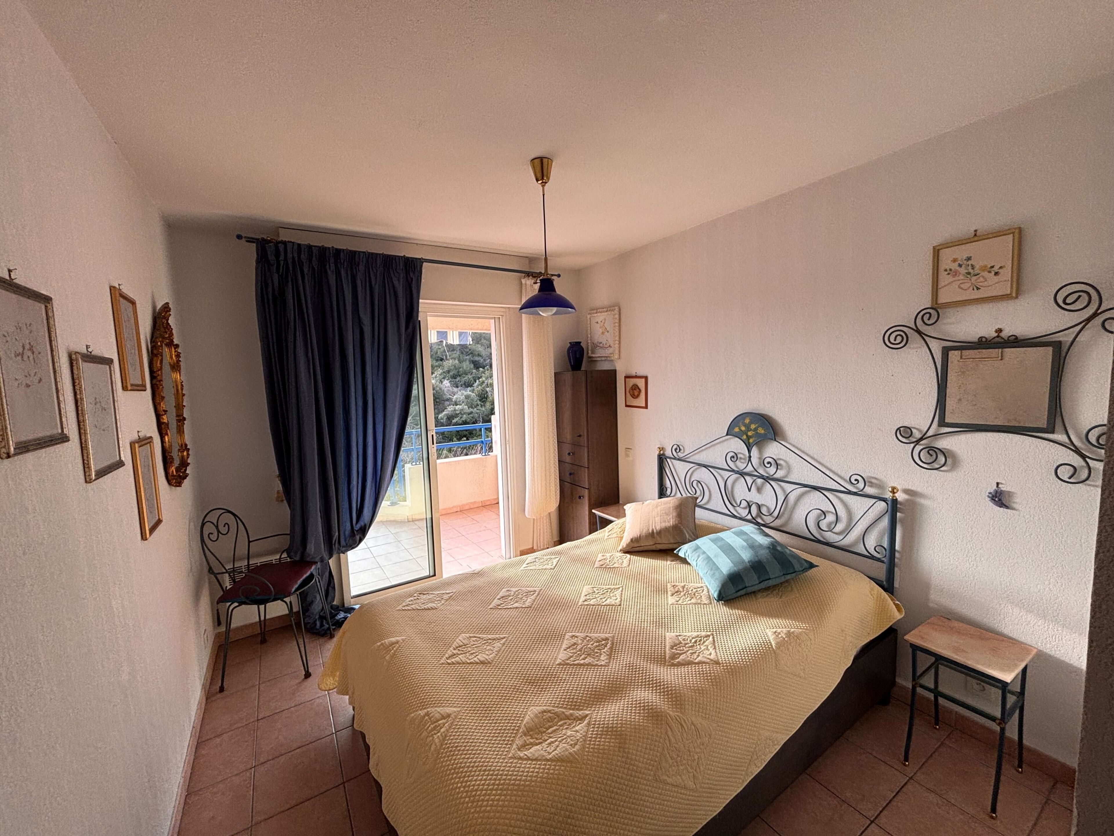 A bedroom with a bed, a chair, a small table, and a balcony with a view.