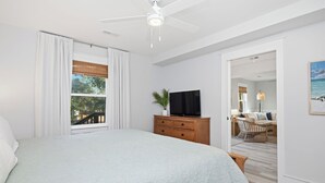 Een slaapkamer met een groot bed, een plafondventilator, een televisie op een houten dressoir en uitzicht op het landschap door een raam.