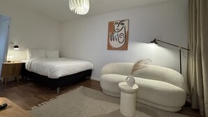 Ein modernes Schlafzimmer mit Bett, Nachttisch, Lampe, Kunstwerk und einer außergewöhnlichen Stehlampe.