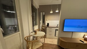 Eine moderne Küche mit Fernseher, der eine Strandansicht zeigt, einem Essbereich mit Tisch und Stühlen sowie einem Holzschrank.