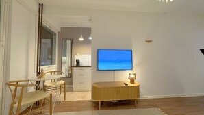 Ein modernes Wohnzimmer mit Flachbildfernseher, Holzmöbeln und einer Küche im Hintergrund.