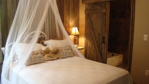 Una cama con dosel, una mesita de noche con lámpara y una puerta de madera rústica.