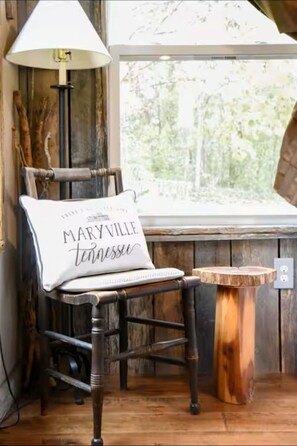 A rustic wooden chair with a cushion that reads "MARYVILLE tennessee" by a window with a view of trees. - Rocky Creek Cottage ~A charming 2-bedroom country cottage in beautiful Maryville (Maryville)