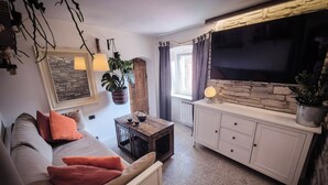 A cozy living room with a sofa, a coffee table, and a TV on a stone wall. - Artist's Refuge (Cerri)