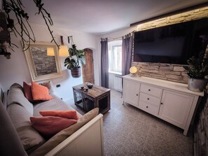 Ein gemütliches Wohnzimmer mit einer Couch, einem Couchtisch und einem Fernseher an einer Steinwand.