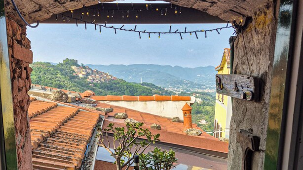 A balcony with a view of a hillside town, a bottle of wine, and two glasses on a table. - Artist's Refuge (Cerri)