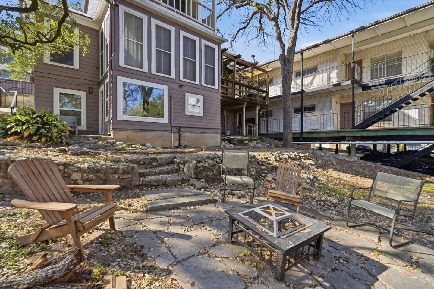 A patio with stone flooring, wooden chairs, and a fire pit.
