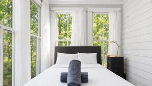 Une chambre avec un grand lit, du linge de lit blanc et deux serviettes enroulées. On y trouve une table de chevet avec une lampe et un tiroir.