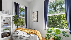 Une chambre à coucher avec un lit, une bibliothèque, une plante en pot et une fenêtre avec des rideaux.
