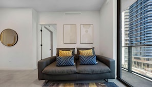 A modern living room with a grey sofa, two patterned cushions, a round mirror, and abstract wall art. - Luxury Downtown Miami 1BR + Den | Pool & Gym (Miami)