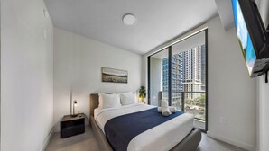 Une chambre d’hôtel moderne dotée d’un grand lit, d’une table de chevet, d’une commode, d’un téléviseur fixé au mur et d’une fenêtre donnant sur la ville.
