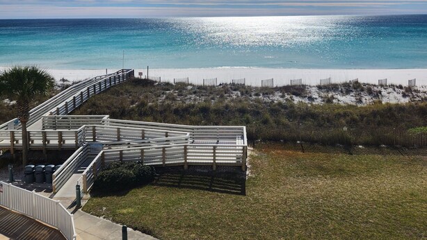 A beach with a wooden boardwalk and a grassy area leading to the water. - Regency Towers #402W Beach Front Condo, Balcony, Pool, Pickleball , Sleeps 8 (gulfbreeze)