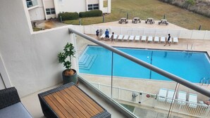 A balcony with wicker furniture, a pool, and a view of the surrounding area. - Regency Towers #402W Beach Front Condo, Balcony, Pool, Pickleball , Sleeps 8 (gulfbreeze)