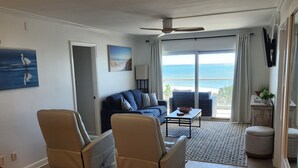 A living room with two recliner chairs, a sofa, a coffee table, and a view of the ocean through large windows. - Regency Towers #402W Beach Front Condo, Balcony, Pool, Pickleball , Sleeps 8 (gulfbreeze)