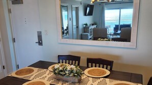 A dining area with a large table, four chairs, and a central floral arrangement. A mirror hangs above the table, reflecting the room. - Regency Towers #402W Beach Front Condo, Balcony, Pool, Pickleball , Sleeps 8 (gulfbreeze)