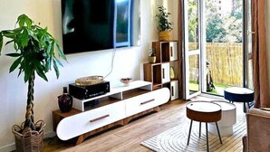 Een moderne woonkamer met een flatscreen-televisie, houten vloeren, een groot raam met uitzicht en een plafondlamp.