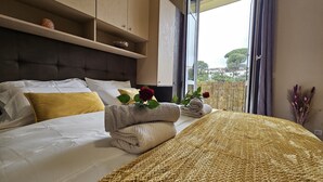 Een hotelkamer met een bed, een hoofdbord, een raam met gordijnen en uitzicht op groen.