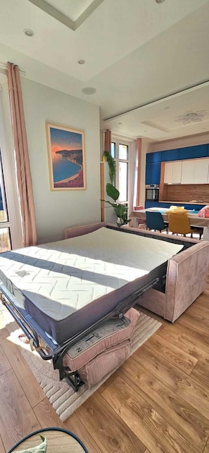 A room with a pull-out bed, a dining area, a kitchen, and a large window with curtains. - Central Cannes Modern T4 - Walk to Beach, Congress (Cannes)