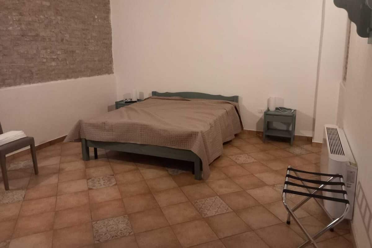 A small, simple room with a bed, a chair, a nightstand, and a radiator.
