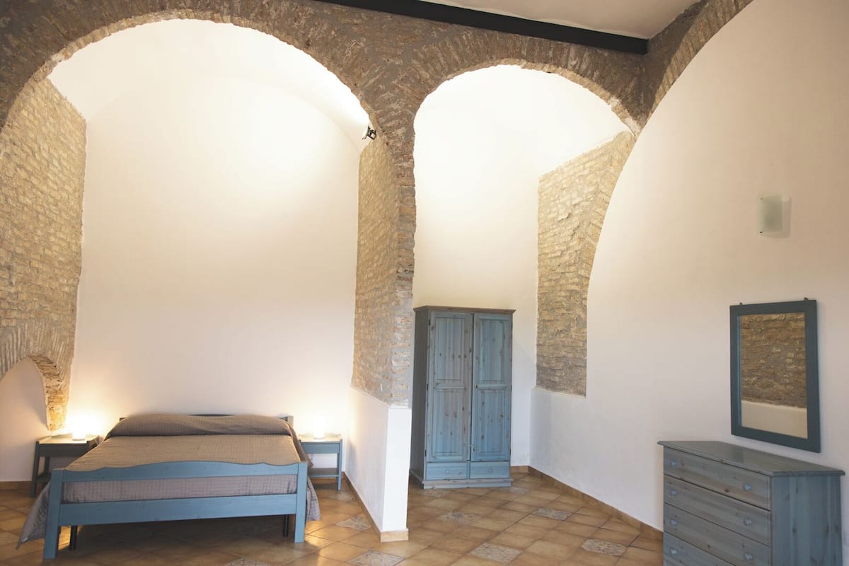 A bedroom with a bed, a dresser, and a wardrobe under a stone archway.