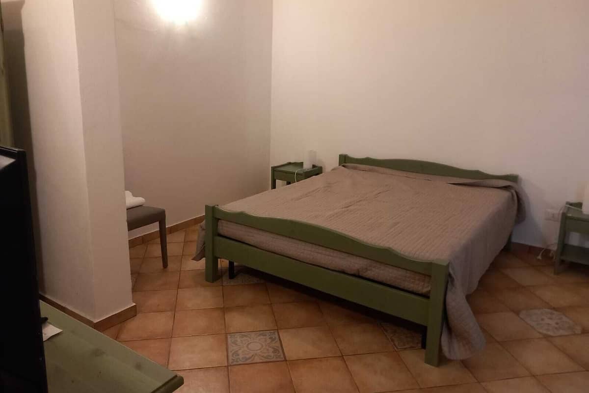 A small, simple bedroom with a single bed, a nightstand, and a chair.