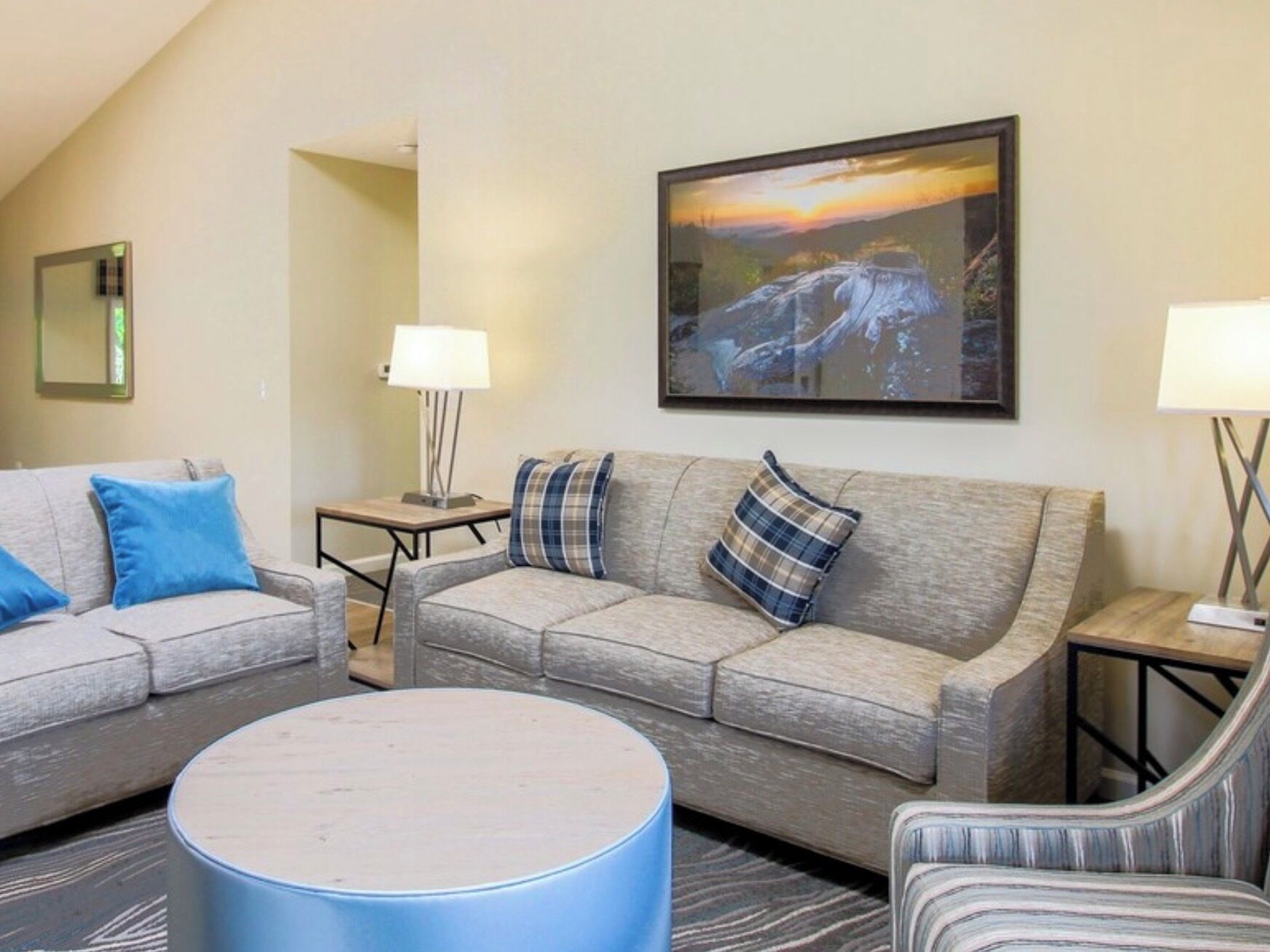Ein modernes Hotelzimmer mit zwei grauen Sofas, einem runden Couchtisch und einem Landschaftsbild.
