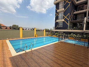 Piscina no terraço com deck de madeira, cercada por grade de metal e plantas em vasos.