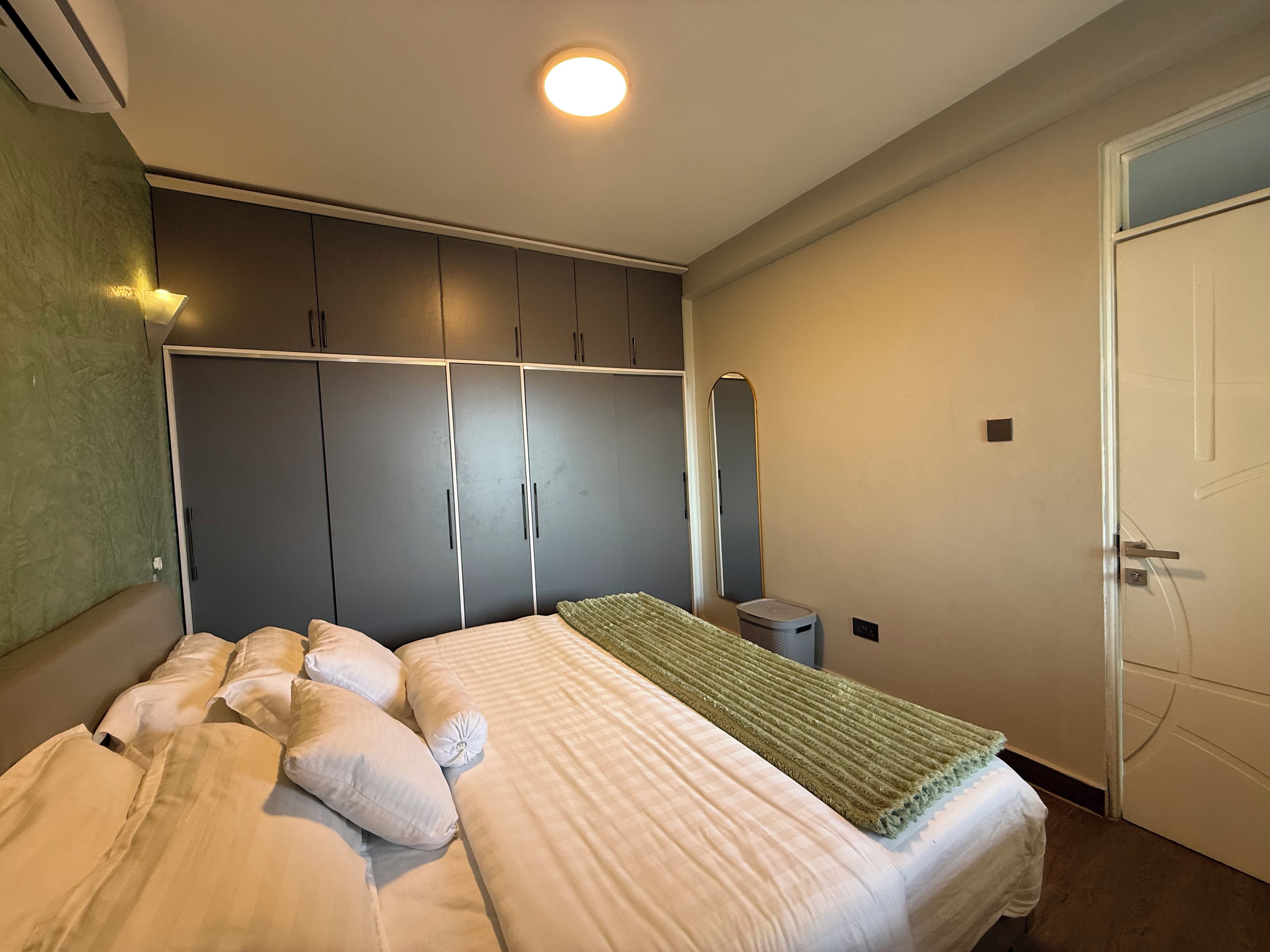 A bedroom with a bed, a wardrobe, a mirror, and a door.