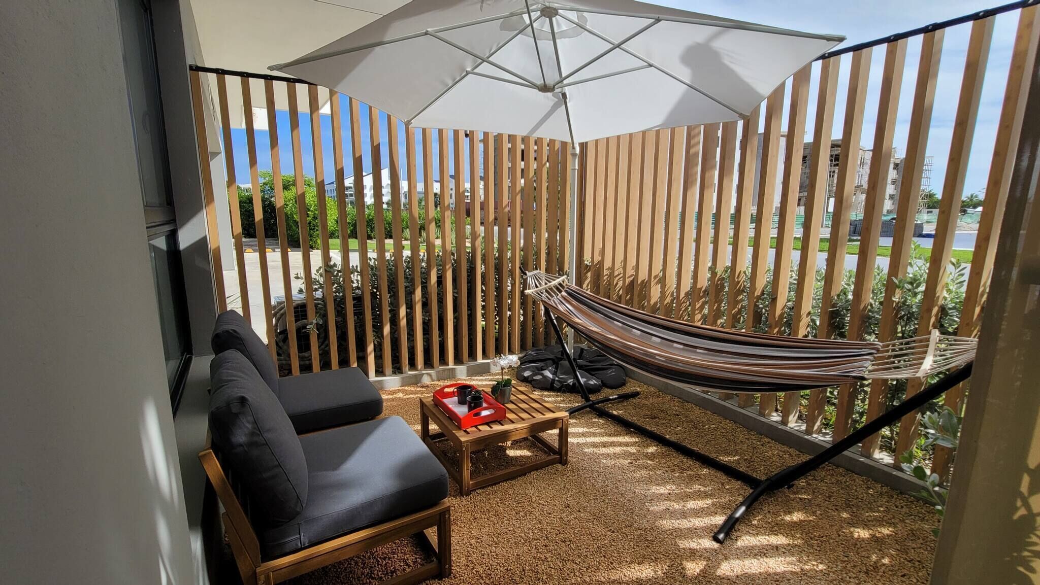 A balcony with a hammock, a black chair, and a small table with a tray of items.