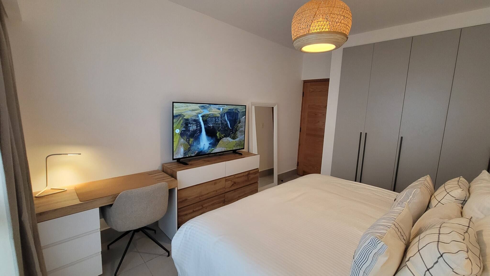 A bedroom with a bed, a desk with a chair, a television, and a wardrobe.