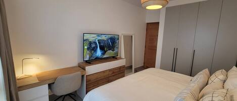 A bedroom with a bed, a desk with a chair, a television, and a wardrobe.