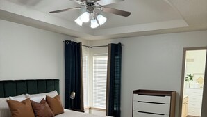Ein Schlafzimmer mit einem Bett, einem Schminktisch, einem Deckenventilator und einem Fenster mit Vorhängen.