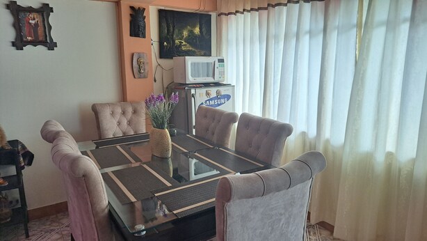 Un coin repas avec une table à plateau en verre, des chaises rembourrées, un vase avec des fleurs et un four à micro-ondes Samsung posé sur un meuble.