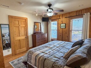 Un dormitorio con cama, cómoda, ventilador de techo y paredes de madera.