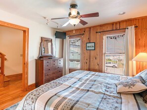 A bedroom with a bed, wooden walls, a ceiling fan, and a window with blinds.