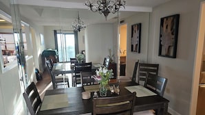 A dining area with a large table, chairs, and a chandelier. There are two side tables with decorative items. The room has a modern design with light-colored walls and wooden flooring. - Charming Ever Green 2-Bedroom Condo in Sugar Mountain with Resort Amenities (Sugar Mountain)