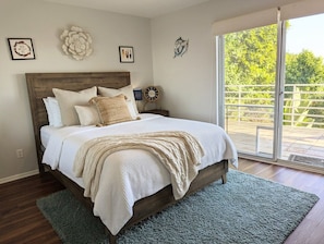 Une chambre avec un lit en bois, un tapis vert, une grande fenĂȘtre donnant sur un paysage verdoyant et des Ćuvres dâart murales.