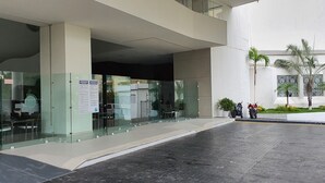 A modern building entrance with glass doors, a sign indicating 'ENTRADA', and a small outdoor seating area with chairs and tables. - Spectacular View: Beachfront Apartment, La Palapa (Acapulco de Juárez)