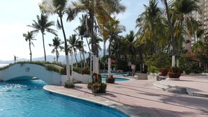 A swimming pool area with palm trees, a bridge, and a view of mountains. - Spectacular View: Beachfront Apartment, La Palapa (Acapulco de Juárez)