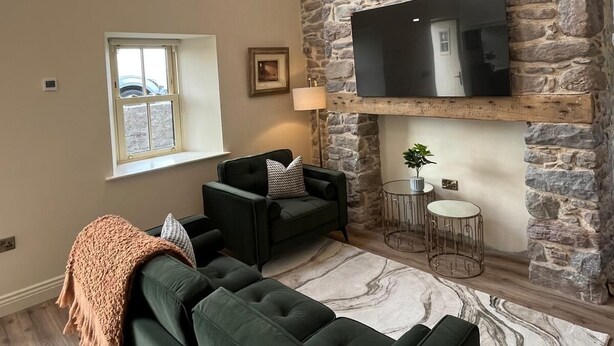 A cozy living room with a stone fireplace, a flat-screen TV, a green sofa set, and a chandelier.
