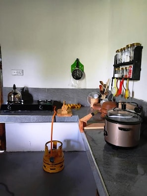 Una cocina con estufa a gas, olla a presión, hervidor y una repisa con frascos y utensilios.