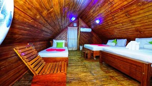 Un dormitorio acogedor en el ático, con paredes de madera, techo inclinado y un ventanal pequeño. Hay dos camas con ropa de cama colorida, un banco de madera y una mesita.