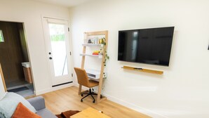 Ett modernt vardagsrum med en grå soffa, ett träbord, en väggmonterad TV och en liten trähylla med dekorativa föremål.